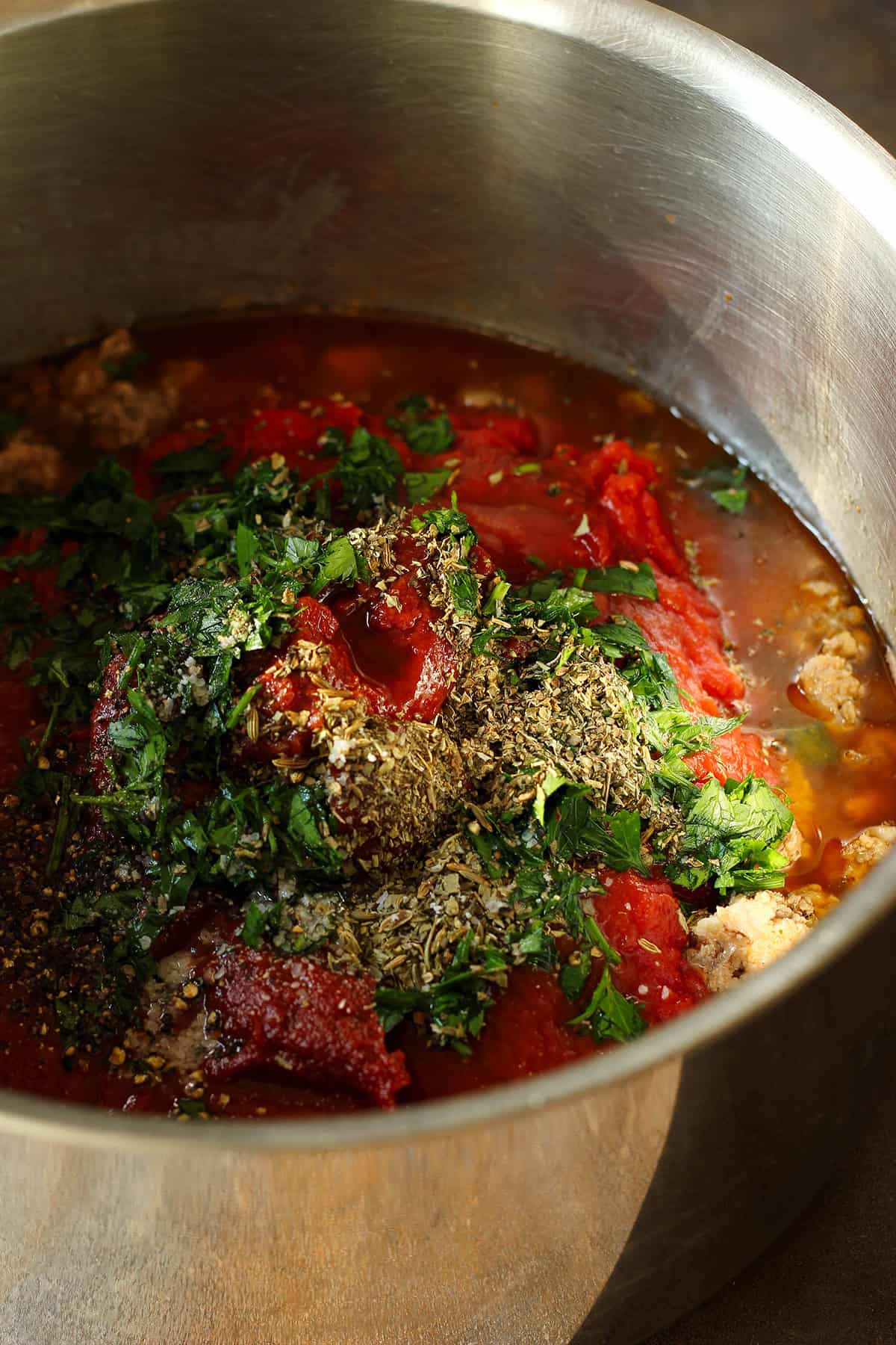 adding herbs and tomatoes to sauce
